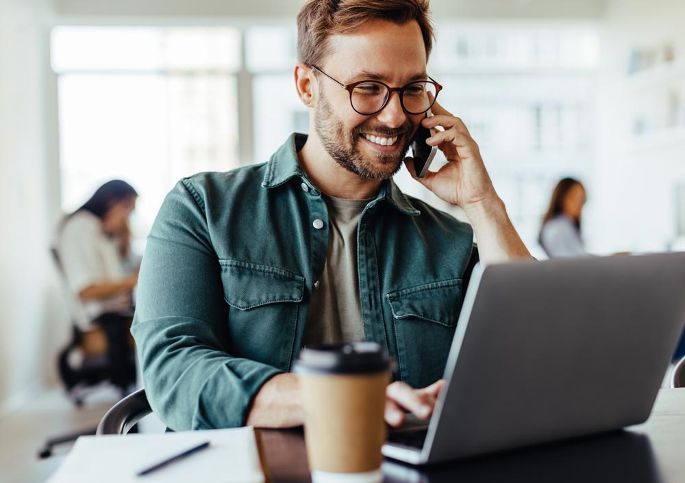 Mann telefoniert am Laptop mit Kaffee (Service/Support)